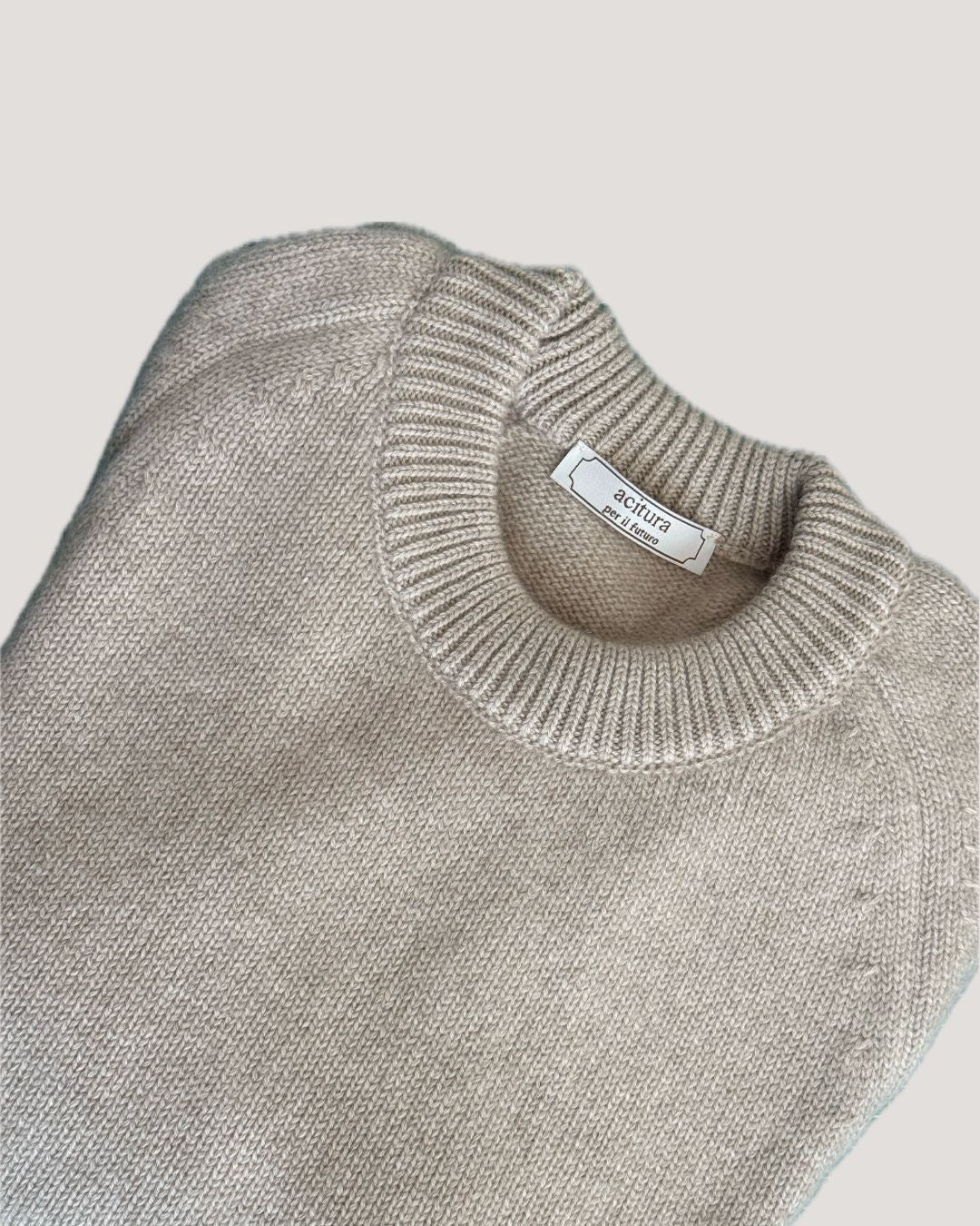 Folded beige sweater with a brand label on a light gray background